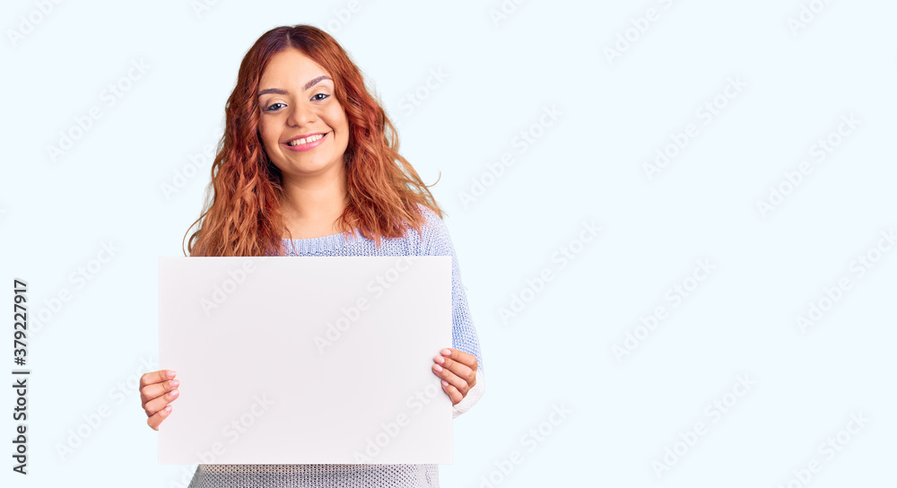 Young latin woman holding blank empty banner looking positive and happy standing and smiling with a confident smile showing teeth Young latin woman holding blank empty banner looking positive and happy standing and smiling with a confident smile showing teeth
