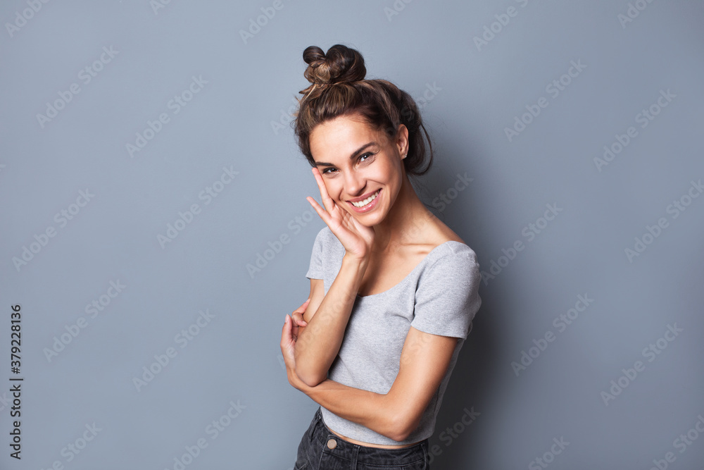 Happy laughing young woman with bun hairstyle and a beautiful smile. Female portrait on a gray. Happy laughing young woman with bun hairstyle and a beautiful smile. Female portrait on a gray.