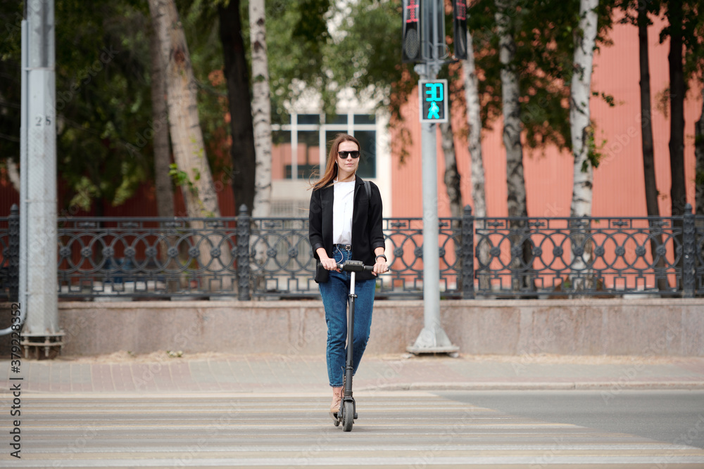 Young elegant woman standing on electric scooter and moving down crosswalk