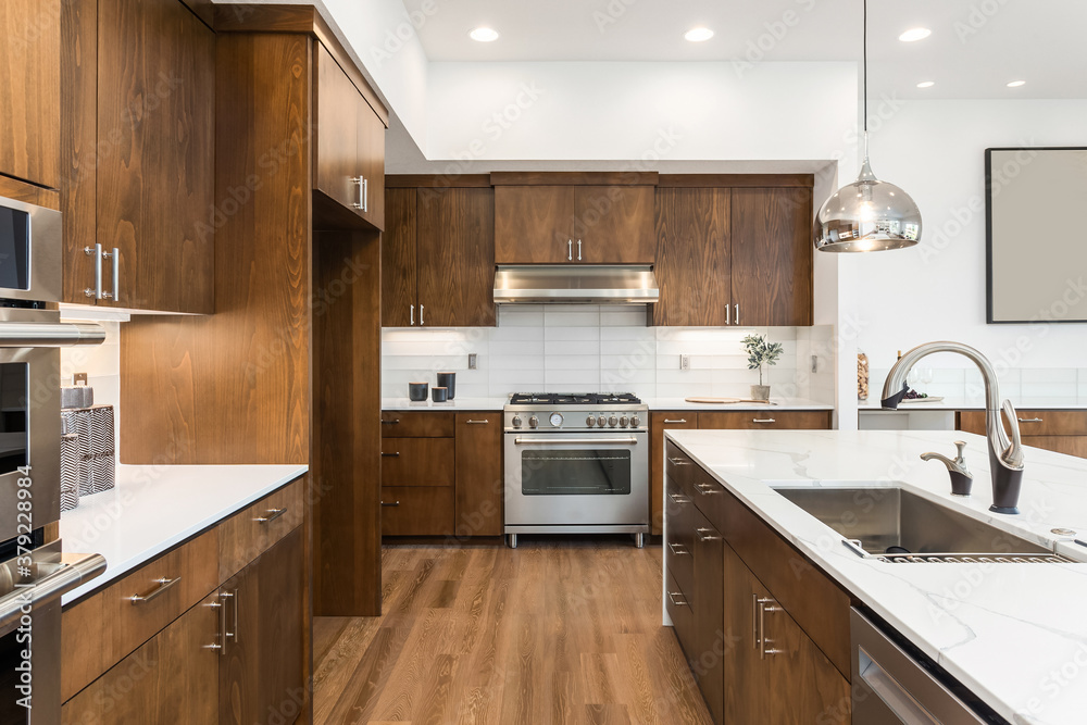 Kitchen in new luxury home with quartz waterfall island, hardwood floors, dark wood cabinets, and stainless steel appliances. Kitchen in new luxury home with quartz waterfall island, hardwood floors, dark wood cabinets, and stainless steel appliances.