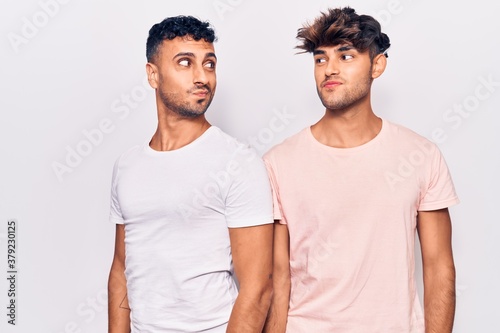 Young gay couple wearing casual clothes smiling looking to the side and staring away thinking.