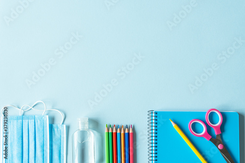 School supplies and coronavirus prevention items on blue background.