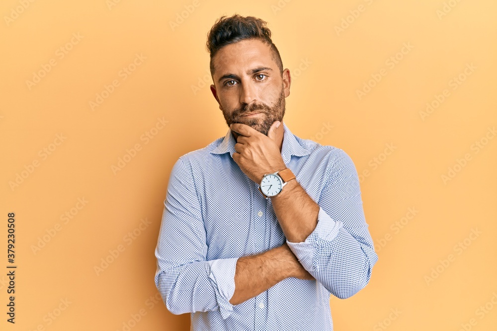 Handsome man with beard wearing casual clothes serious face thinking about question with hand on chin, thoughtful about confusing idea Handsome man with beard wearing casual clothes serious face thinking about question with hand on chin, thoughtful about confusing idea