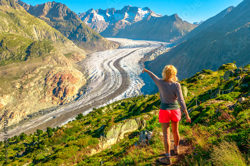 Aletsch Glacier from Moosfluh viewpoint in summer, Valais Canton, Switzerland, Europe. Tourist hiker woman pointed the Alpine glacier. Outdoor activities. Trekking in Swiss Alps. photo