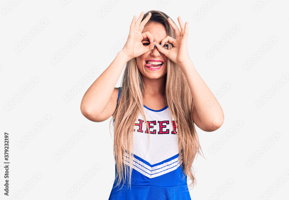 Young beautiful blonde woman wearing cheerleader uniform doing ok gesture like binoculars sticking tongue out, eyes looking through fingers. crazy expression. Young beautiful blonde woman wearing cheerleader uniform doing ok gesture like binoculars sticking tongue out, eyes looking through fingers. crazy expression.