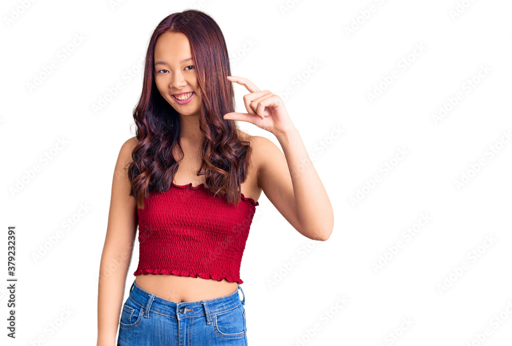 Young beautiful chinese girl wearing casual clothes smiling and confident gesturing with hand doing small size sign with fingers looking and the camera. measure concept. Young beautiful chinese girl wearing casual clothes smiling and confident gesturing with hand doing small size sign with fingers looking and the camera. measure concept.