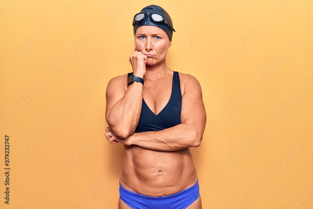 Middle age caucasian blonde woman wearing bikini,  swimming cap and diving googles thinking looking tired and bored with depression problems with crossed arms.