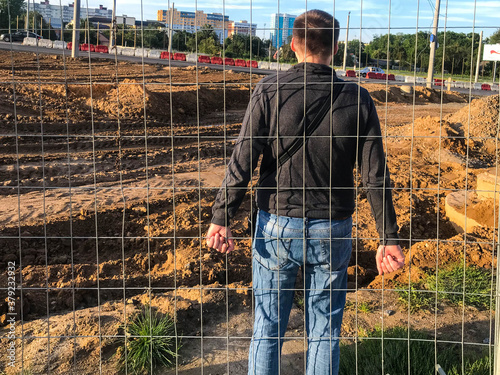 a young strong guy stands behind a metal fence and holds his fingers to it. protest mood. rally. the guy refuses to leave, there is resistance. holding onto bars