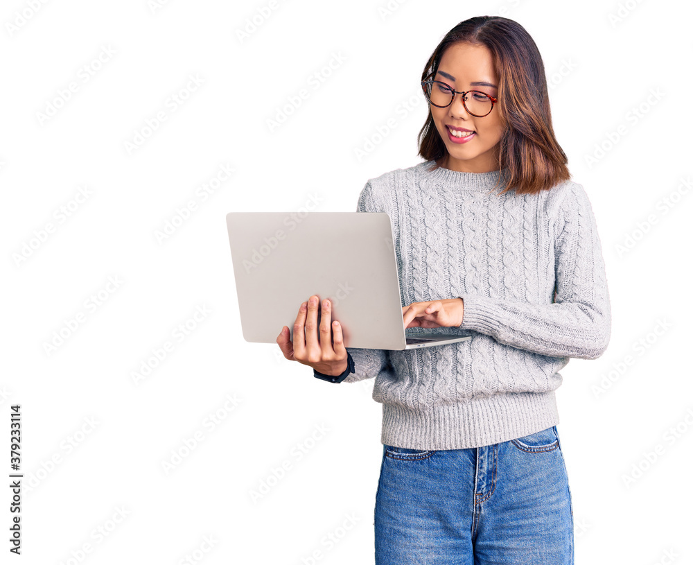 Young beautiful chinese girl wearing glasses holding laptop looking positive and happy standing and smiling with a confident smile showing teeth Young beautiful chinese girl wearing glasses holding laptop looking positive and happy standing and smiling with a confident smile showing teeth