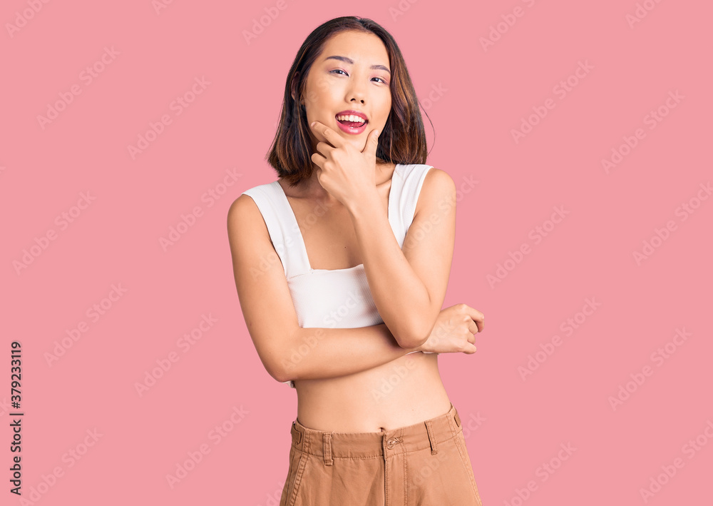 Young beautiful chinese girl wearing casual clothes looking confident at the camera smiling with crossed arms and hand raised on chin. thinking positive.