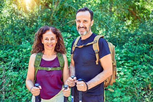 Beautiful couple of hiker wearing backpack smiling happy. Standing with smile on face doing trekking using hiking stick at forest