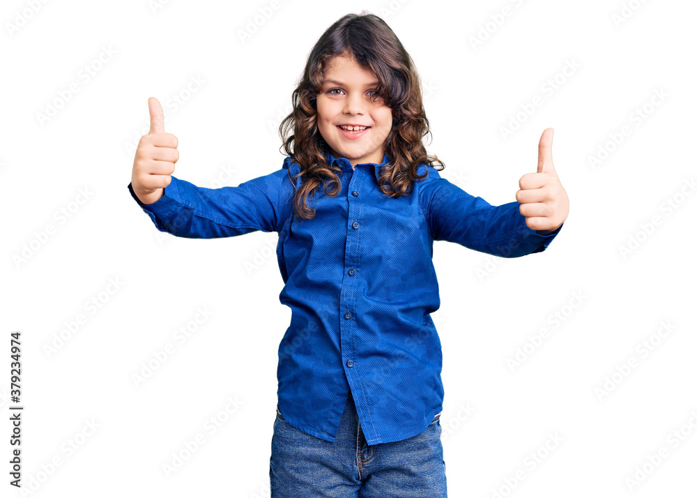 Cute child with long hair wearing casual clothes approving doing positive gesture with hand, thumbs up smiling and happy for success. winner gesture. Cute child with long hair wearing casual clothes approving doing positive gesture with hand, thumbs up smiling and happy for success. winner gesture.