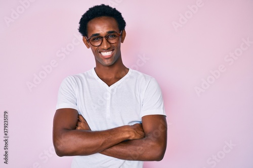 African handsome man wearing casual clothes and glasses happy face smiling with crossed arms looking at the camera. positive person.