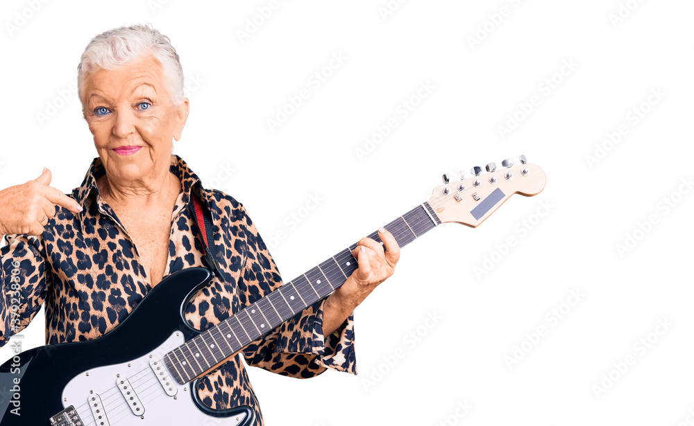 Senior beautiful woman with blue eyes and grey hair with modern look playing electric guitar pointing finger to one self smiling happy and proud