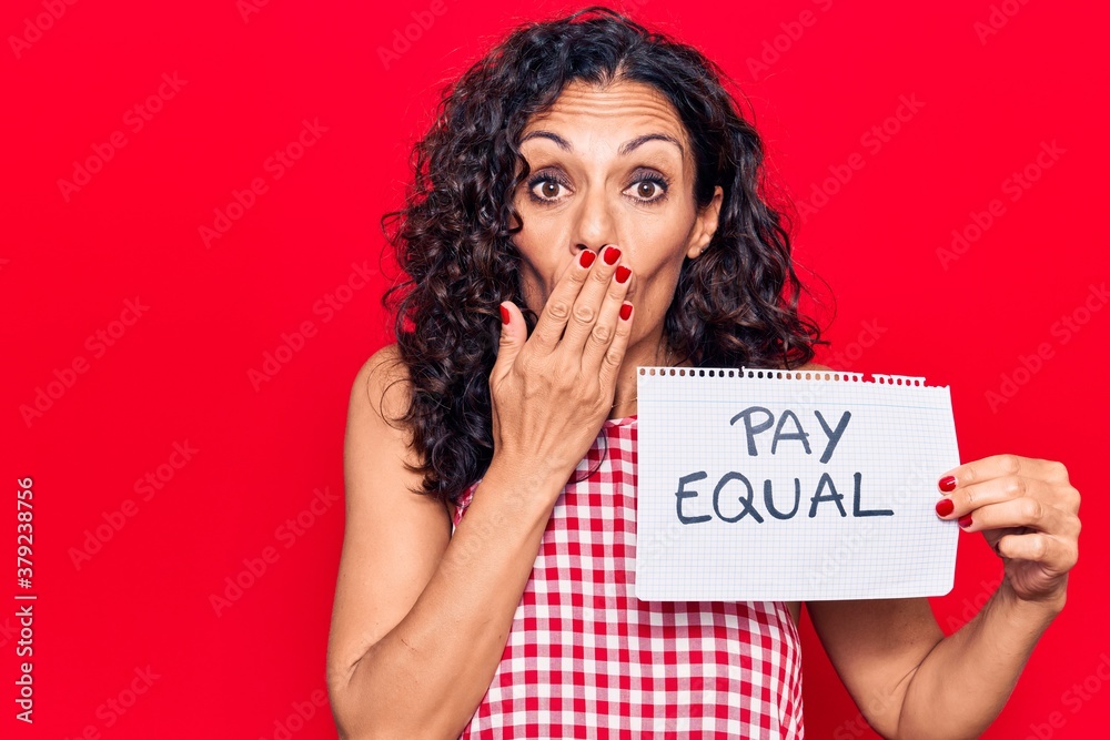 Middle age beautiful woman holding pay equal paper covering mouth with hand, shocked and afraid for mistake. surprised expression