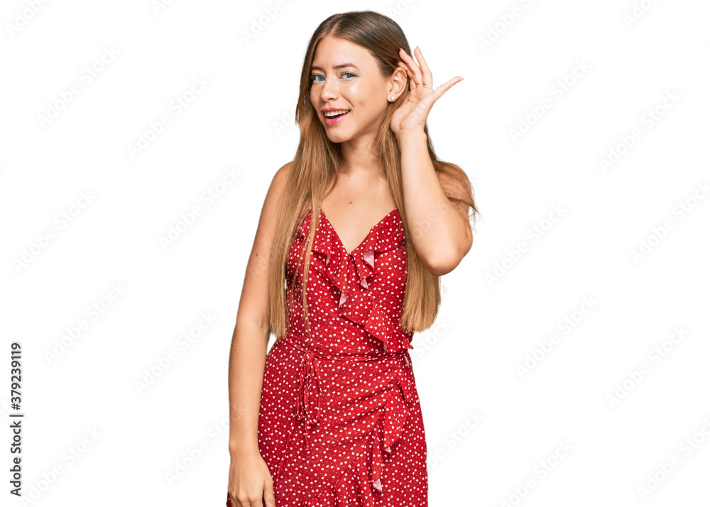 Beautiful blonde woman wearing summer dress smiling with hand over ear listening an hearing to rumor or gossip. deafness concept. Beautiful blonde woman wearing summer dress smiling with hand over ear listening an hearing to rumor or gossip. deafness concept.