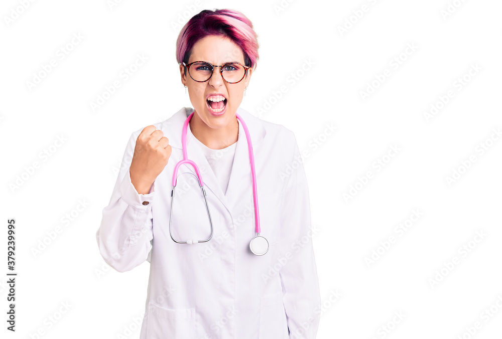 Young beautiful woman with pink hair wearing doctor uniform angry and mad raising fist frustrated and furious while shouting with anger. rage and aggressive concept. Young beautiful woman with pink hair wearing doctor uniform angry and mad raising fist frustrated and furious while shouting with anger. rage and aggressive concept.