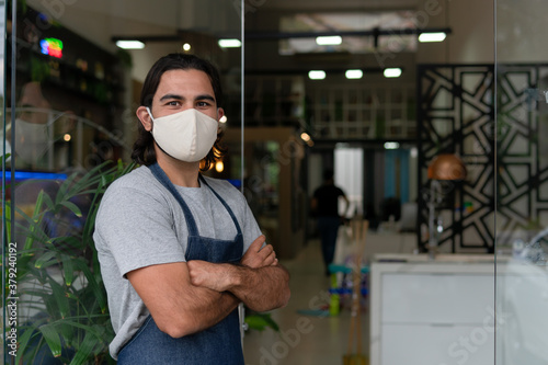 Friendly latin male entrepreneur with crossed arms looking at camera in front of store facade. business, workplace, successful, entrepreneur, occupation concept..