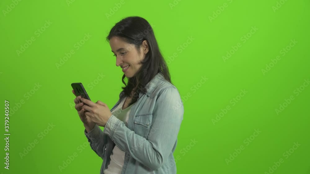 Portrait of casual woman showing smartphone to camera with smile at green screen background. Portrait shot at green screen studio.
Portrait of casual woman showing smartphone to camera with smile at green screen background. Portrait shot at green screen studio.