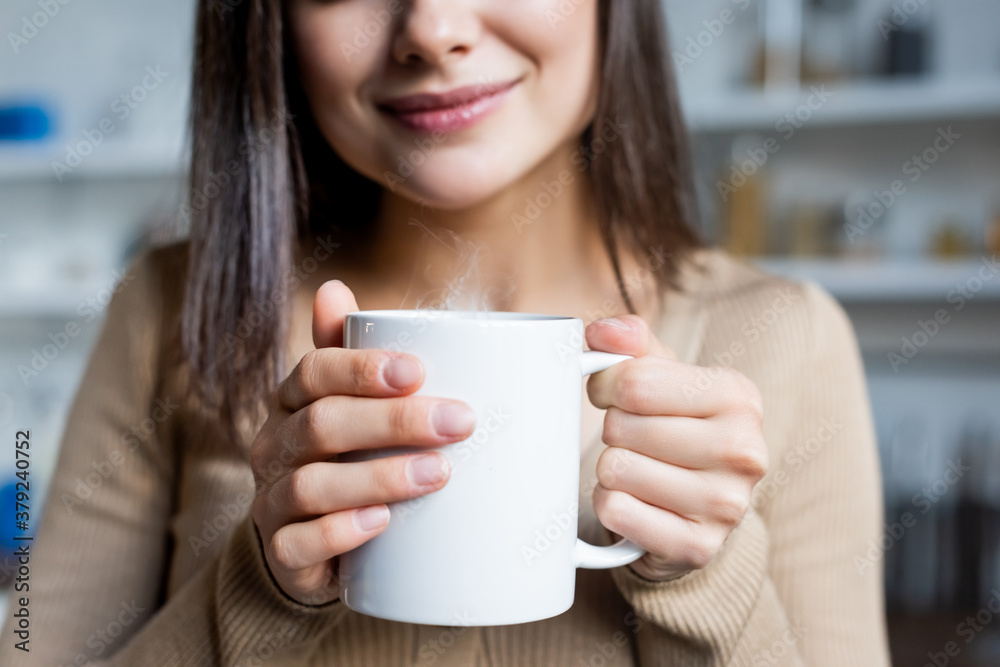 cropped view of pleased young woman holding cup of warm drink at home cropped view of pleased young woman holding cup of warm drink at home