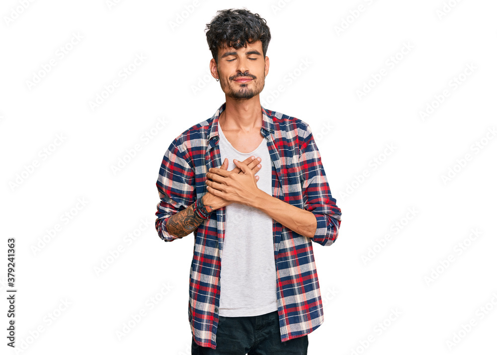 Young hispanic man wearing casual clothes smiling with hands on chest with closed eyes and grateful gesture on face. health concept. Young hispanic man wearing casual clothes smiling with hands on chest with closed eyes and grateful gesture on face. health concept.