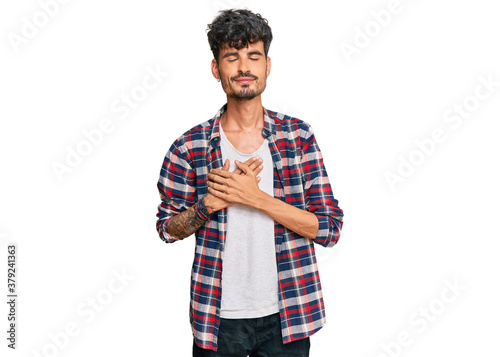 Young hispanic man wearing casual clothes smiling with hands on chest with closed eyes and grateful gesture on face. health concept.