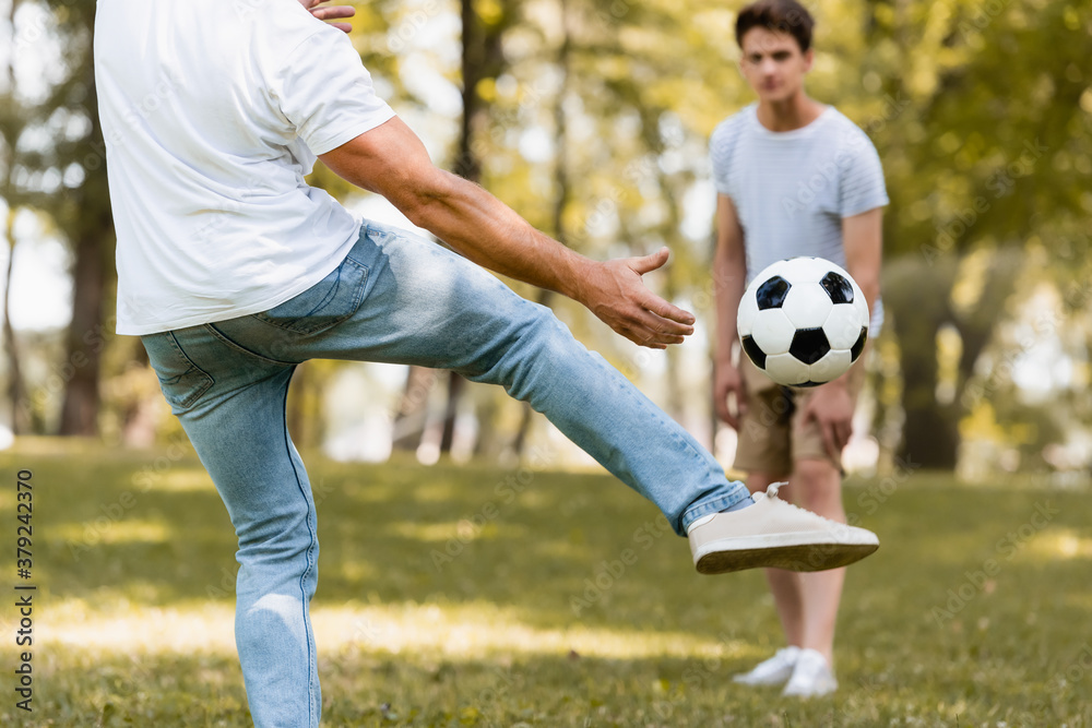 selective focus of father kicking football near teenager son