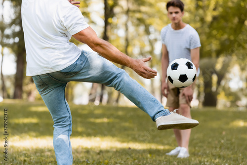 selective focus of father kicking football near teenager son © LIGHTFIELD STUDIOS