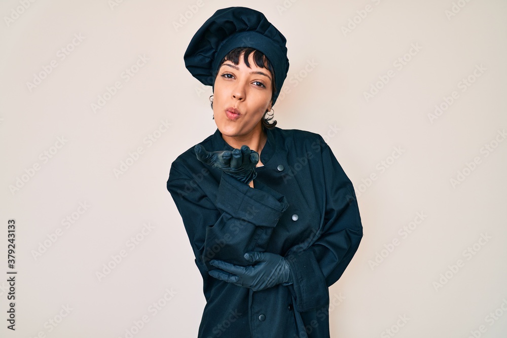 Beautiful brunettte woman wearing professional cook uniform looking at the camera blowing a kiss with hand on air being lovely and sexy. love expression. Beautiful brunettte woman wearing professional cook uniform looking at the camera blowing a kiss with hand on air being lovely and sexy. love expression.