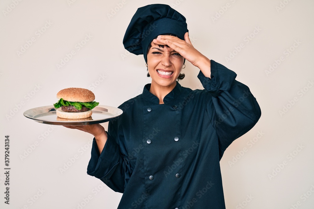 Beautiful brunettte woman chef holding burguer stressed and frustrated with hand on head, surprised and angry face