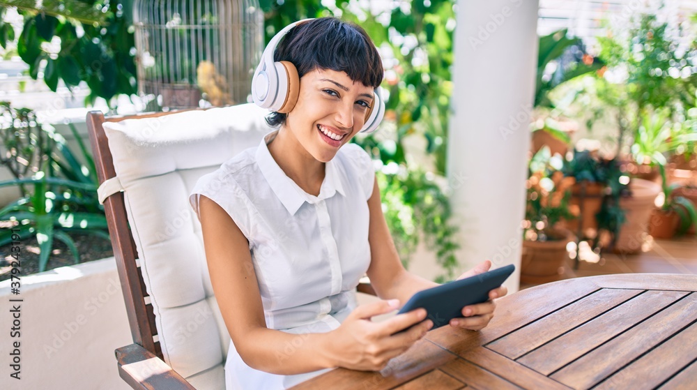 Beautiful woman with short hair sitting at the terrace on a sunny day wearing headphones using touchpad device Beautiful woman with short hair sitting at the terrace on a sunny day wearing headphones using touchpad device
