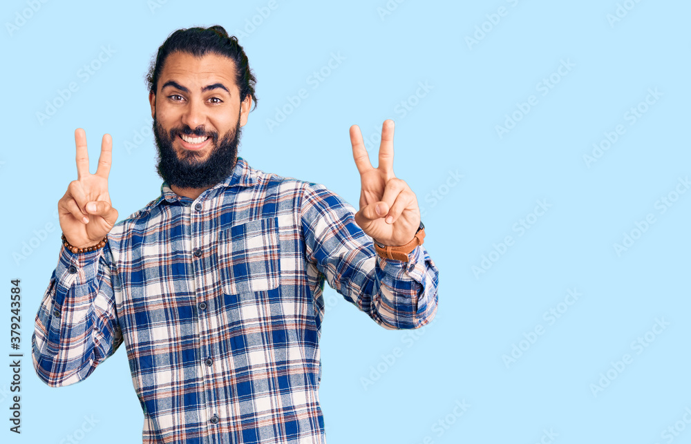 Young arab man wearing casual clothes smiling looking to the camera showing fingers doing victory sign. number two. Young arab man wearing casual clothes smiling looking to the camera showing fingers doing victory sign. number two.