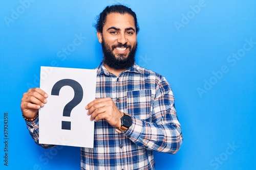 Young arab man holding question mark looking positive and happy standing and smiling with a confident smile showing teeth © Krakenimages.com