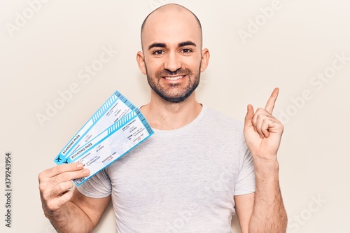 Young handsome bald man holding airline boarding pass smiling happy pointing with hand and finger to the side photo