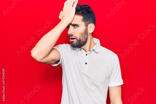 Young handsome man with beard wearing casual polo surprised with hand on head for mistake, remember error. forgot, bad memory concept.