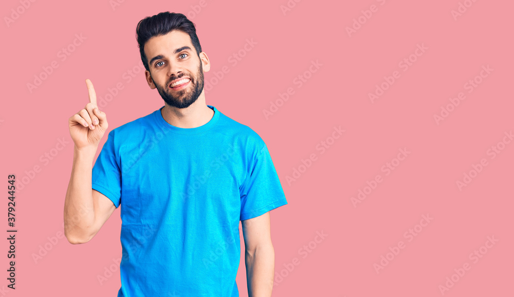 Young handsome man with beard wearing casual t-shirt pointing finger up with successful idea. exited and happy. number one. Young handsome man with beard wearing casual t-shirt pointing finger up with successful idea. exited and happy. number one.