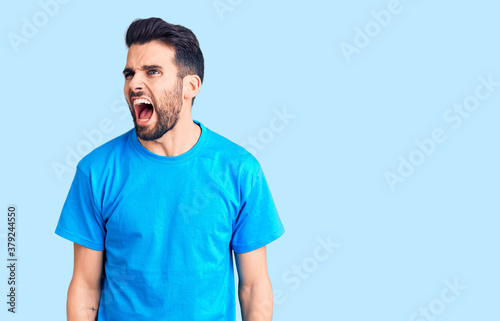 Young handsome man with beard wearing casual t-shirt angry and mad screaming frustrated and furious  shouting with anger. rage and aggressive concept.