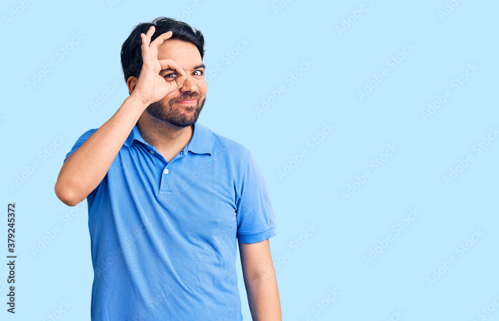 Fototapeta premium Young hispanic man wearing casual clothes doing ok gesture with hand smiling, eye looking through fingers with happy face.