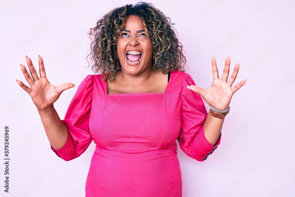 Young african american plus size woman wearing casual clothes crazy and mad shouting and yelling with aggressive expression and arms raised. frustration concept. Young african american plus size woman wearing casual clothes crazy and mad shouting and yelling with aggressive expression and arms raised. frustration concept.