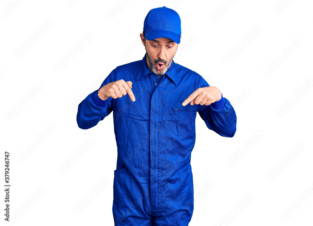 Middle age handsome man wearing mechanic uniform pointing down with fingers showing advertisement, surprised face and open mouth