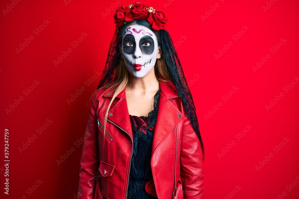 Woman wearing day of the dead costume over red making fish face with lips, crazy and comical gesture. funny expression. Woman wearing day of the dead costume over red making fish face with lips, crazy and comical gesture. funny expression.