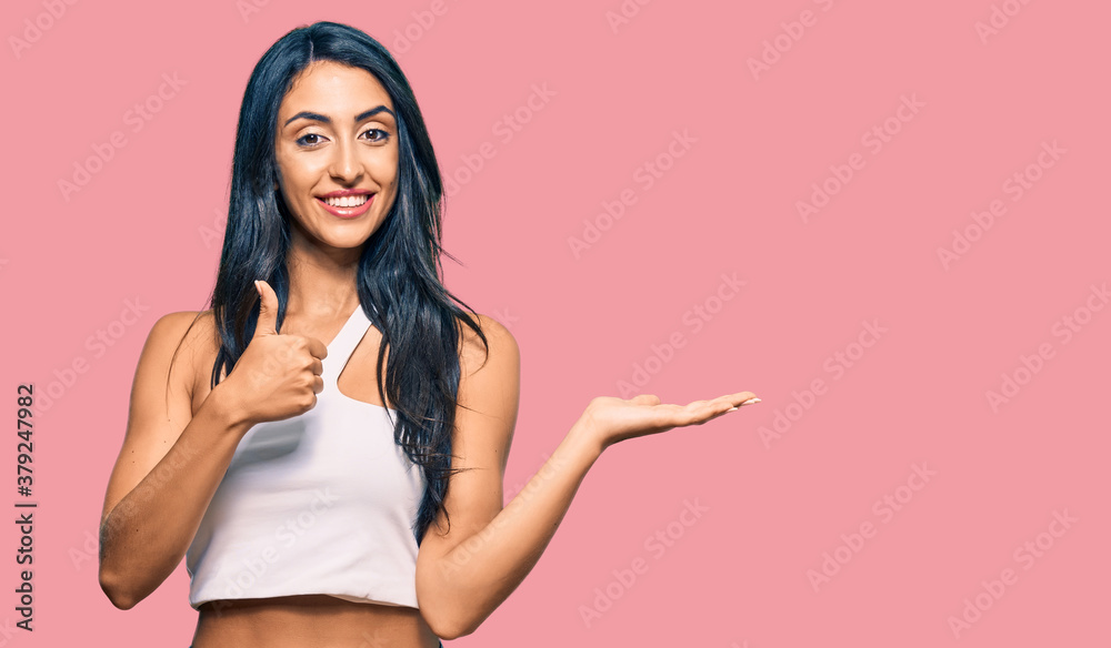 Beautiful hispanic woman wearing casual clothes showing palm hand and doing ok gesture with thumbs up, smiling happy and cheerful Beautiful hispanic woman wearing casual clothes showing palm hand and doing ok gesture with thumbs up, smiling happy and cheerful