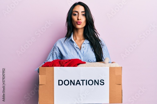 Beautiful hispanic woman volunteer holding donations box looking at the camera blowing a kiss being lovely and sexy. love expression. © Krakenimages.com