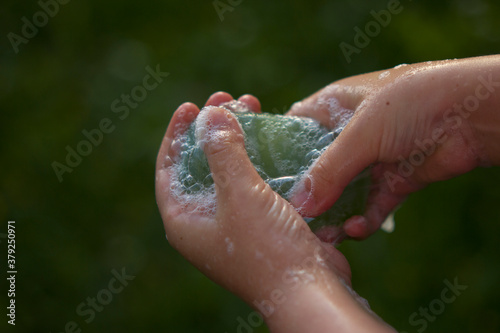 Little girl washing hands with green soap in the garden. Hands hygiene and virus infections prevention.