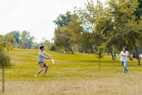 Photography teenager boy holding softball bat and playing baseball with father in green park