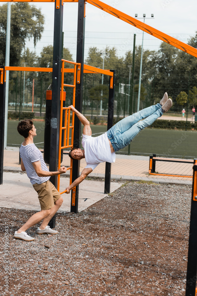 Fototapeta premium teenager son pointing with hand while looking at sportive father exercising on horizontal bars