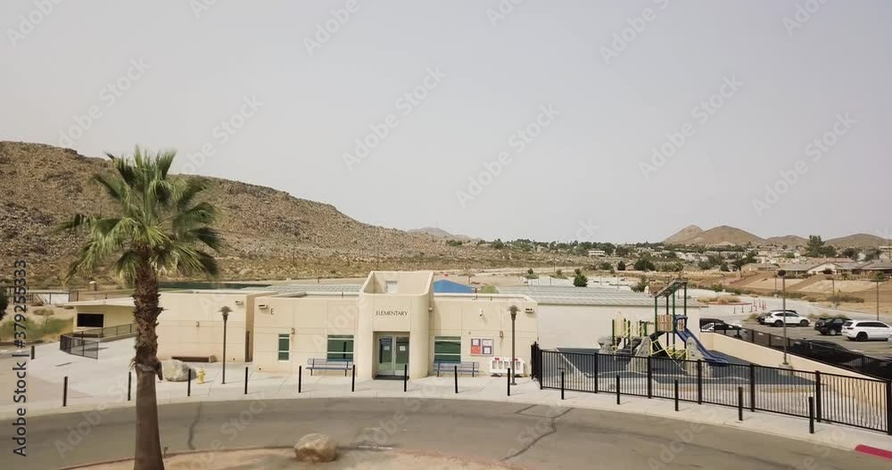 Aerial view of an elementary school with palm trees in the foreground during a pandemic, limited cars in parking lot Aerial view of an elementary school with palm trees in the foreground during a pandemic, limited cars in parking lot