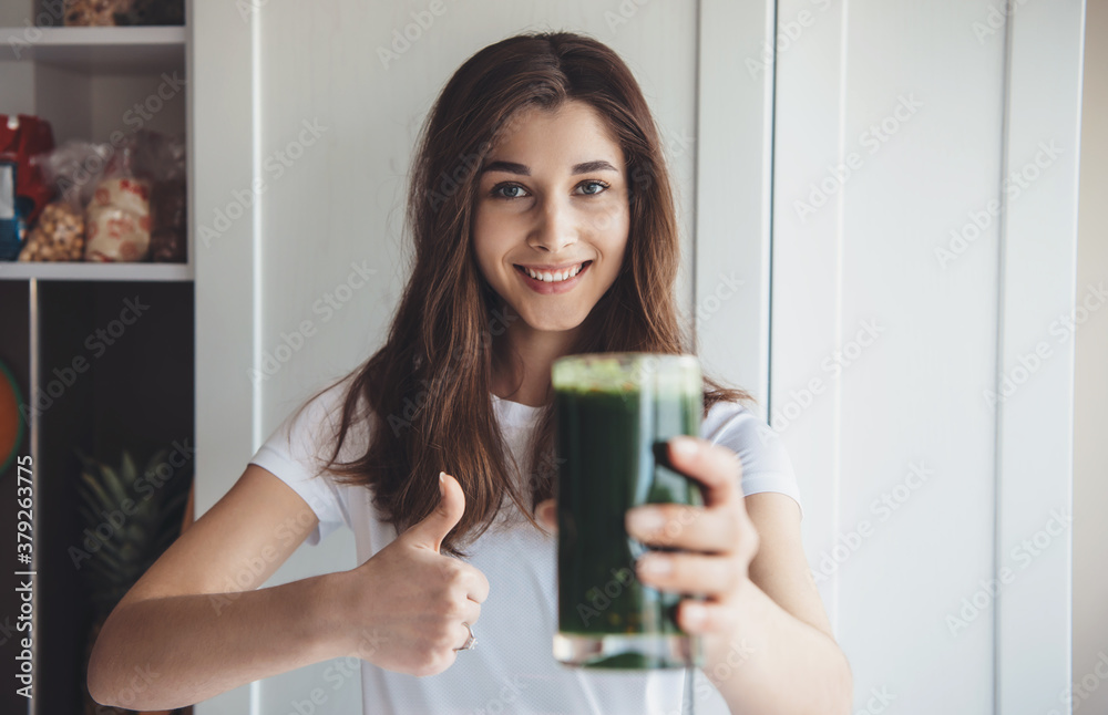Caucasian woman holding a glass with fresh green juice is smiling and gesturing like sign at camera Caucasian woman holding a glass with fresh green juice is smiling and gesturing like sign at camera