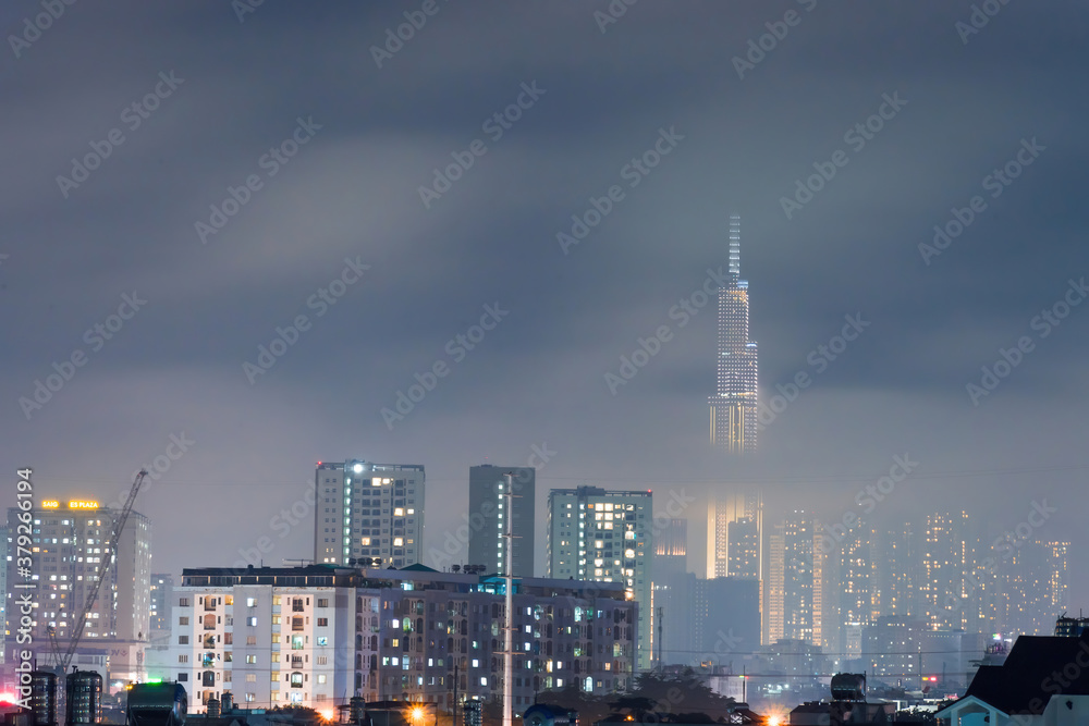Obraz premium Spectacular view of a landmark 81 skyscraper in mist and clouds at Saigon at night in Ho chi minh city, Vietnam