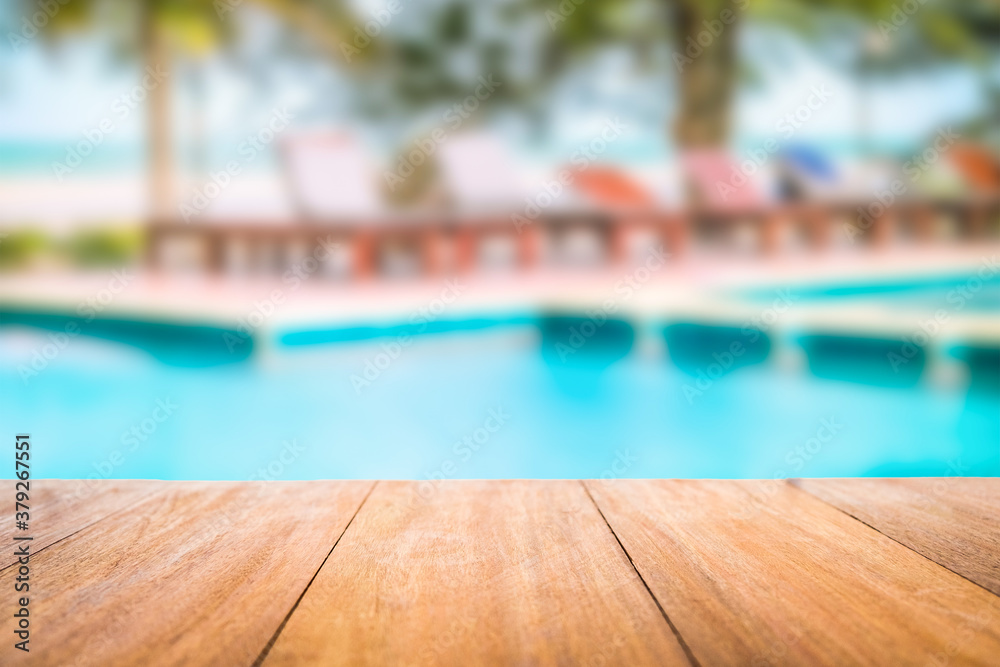 Image of wood table in front of a swimming pool blurred background. Brown wooden desk empty counter in front of the poolside on beautiful beach resort and outdoor spa.